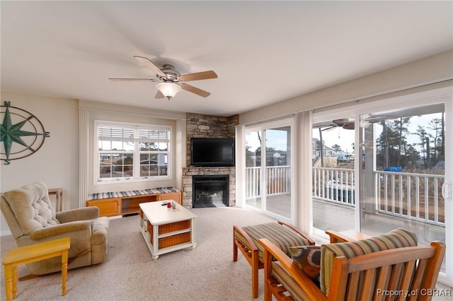 living room with a stone fireplace, plenty of natural light, light colored carpet, and ceiling fan