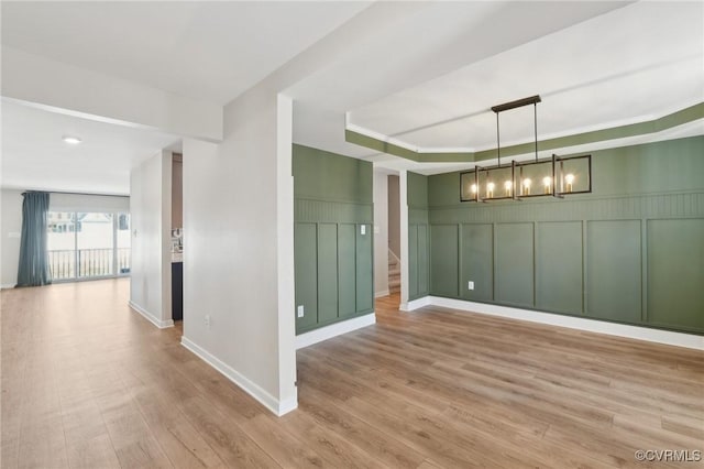 unfurnished dining area with an inviting chandelier, light wood-type flooring, and a tray ceiling