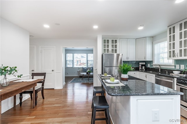 kitchen with appliances with stainless steel finishes, white cabinetry, a center island, decorative backsplash, and light wood-type flooring