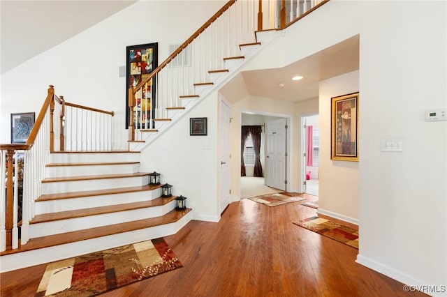 stairway with wood-type flooring and a towering ceiling