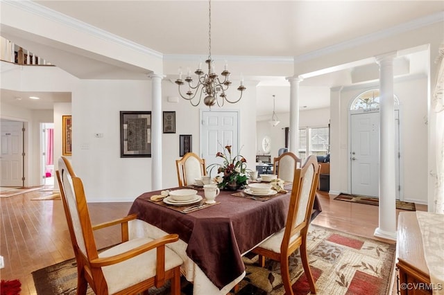 dining room with an inviting chandelier, ornamental molding, decorative columns, and light wood-type flooring