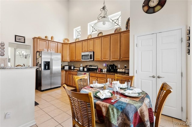 kitchen featuring appliances with stainless steel finishes, a towering ceiling, tasteful backsplash, light tile patterned flooring, and decorative light fixtures