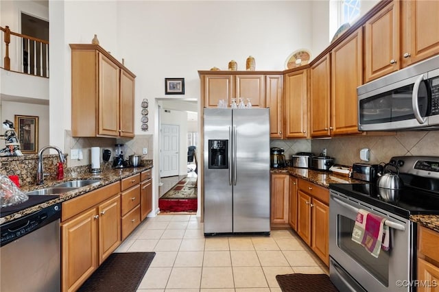 kitchen with sink, a towering ceiling, dark stone counters, and appliances with stainless steel finishes