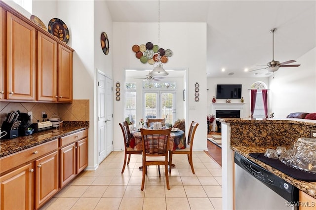 kitchen with light tile patterned floors, ceiling fan, dishwasher, dark stone countertops, and tasteful backsplash