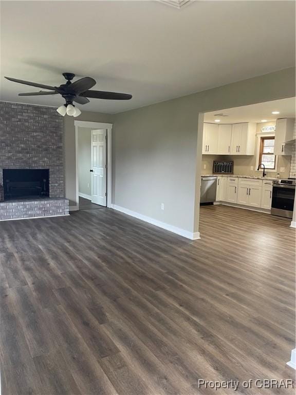 unfurnished living room with dark hardwood / wood-style flooring, sink, a brick fireplace, and ceiling fan