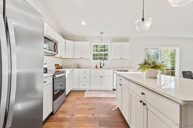 kitchen featuring hanging light fixtures, white cabinetry, appliances with stainless steel finishes, and light hardwood / wood-style flooring