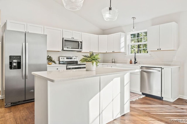 kitchen featuring vaulted ceiling, appliances with stainless steel finishes, decorative light fixtures, white cabinets, and a center island