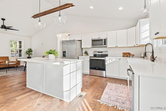 kitchen with white cabinetry, hanging light fixtures, stainless steel appliances, a center island, and light wood-type flooring