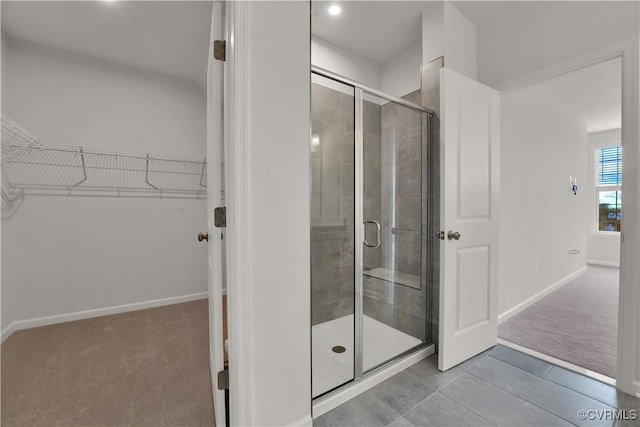 full bathroom with a walk in closet, a shower stall, baseboards, and tile patterned flooring