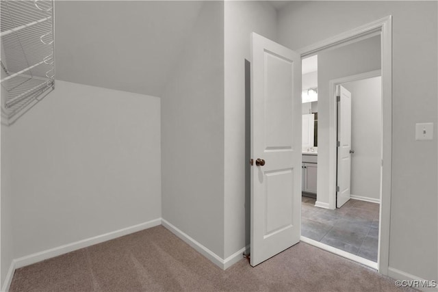 hallway featuring baseboards, lofted ceiling, and carpet