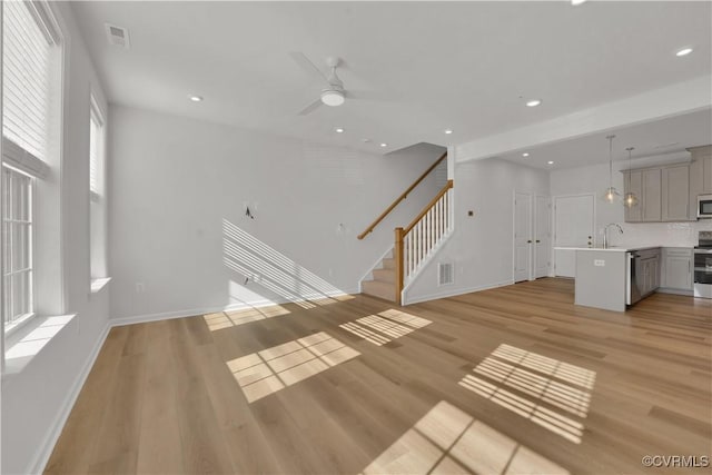 unfurnished living room featuring visible vents, light wood-style flooring, recessed lighting, a sink, and stairs