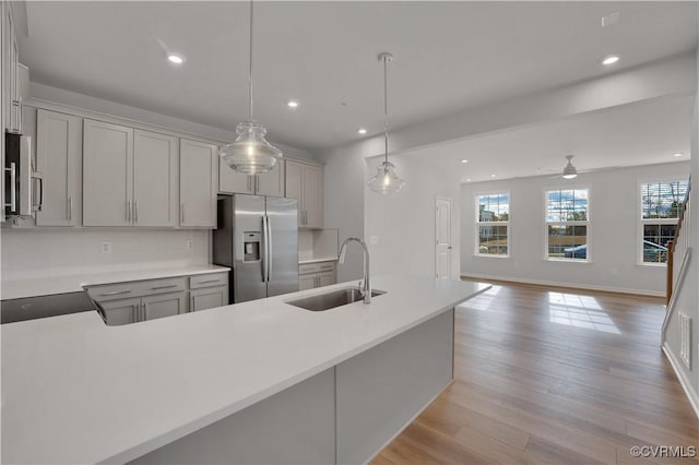 kitchen featuring sink, decorative light fixtures, light wood-type flooring, gray cabinets, and stainless steel appliances