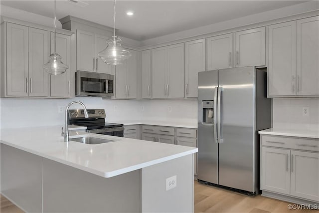 kitchen with gray cabinets, appliances with stainless steel finishes, decorative light fixtures, sink, and light hardwood / wood-style flooring