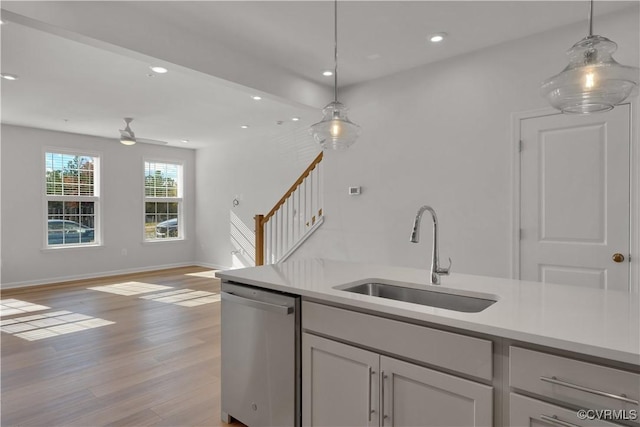 kitchen with hanging light fixtures, a sink, light wood-style flooring, and stainless steel dishwasher