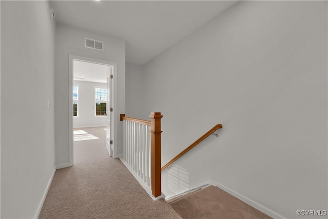 hallway with an upstairs landing, visible vents, carpet floors, and baseboards