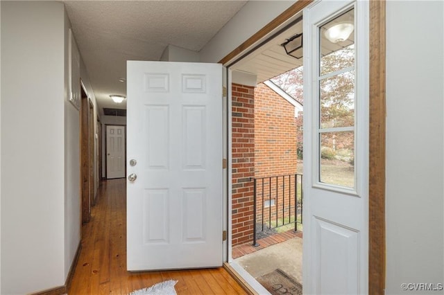 doorway with a textured ceiling and light hardwood / wood-style flooring