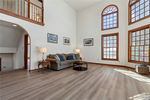 living room featuring arched walkways, a high ceiling, baseboards, and light wood-style floors