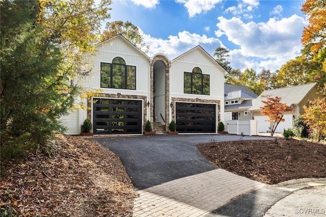 modern inspired farmhouse with driveway, stone siding, and an attached garage