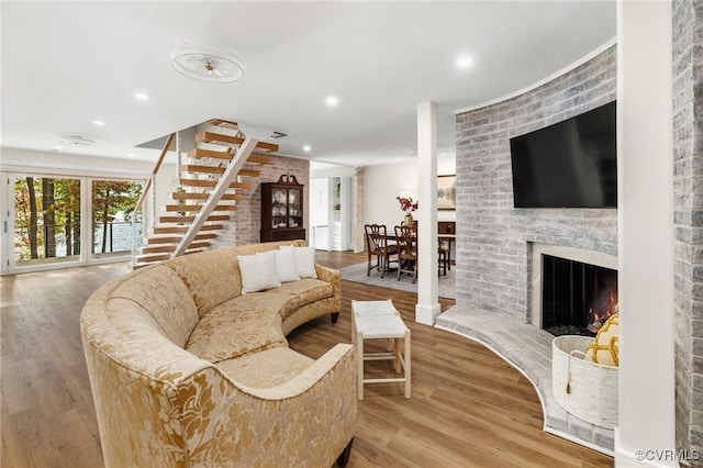 living area with stairs, a brick fireplace, wood finished floors, and recessed lighting