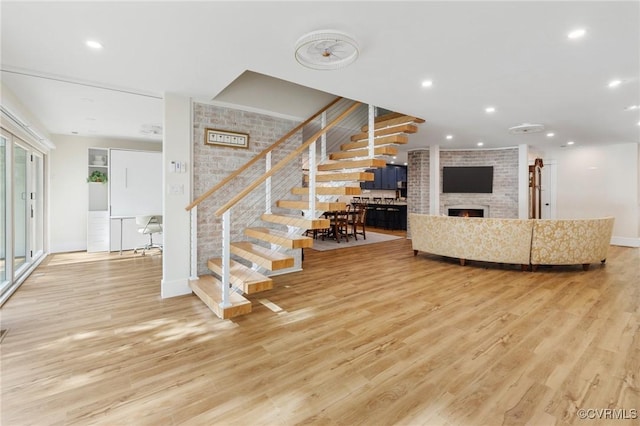 unfurnished living room featuring light wood-style flooring, recessed lighting, brick wall, a fireplace, and stairway