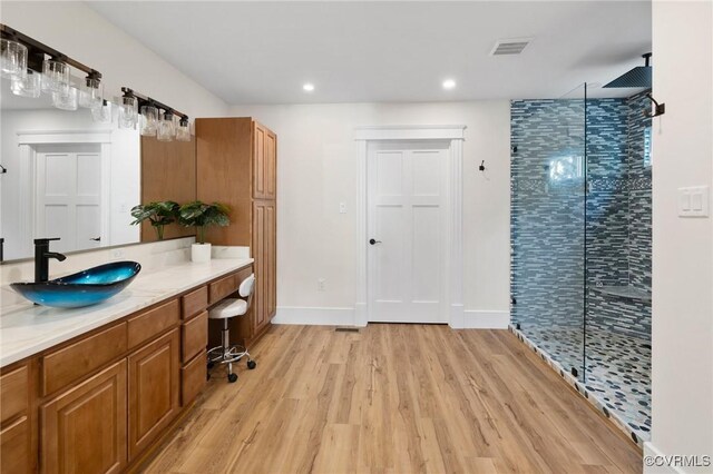 full bathroom featuring wood finished floors, vanity, visible vents, baseboards, and a tile shower