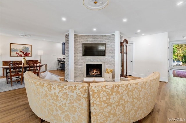 living area featuring recessed lighting, a brick fireplace, baseboards, and wood finished floors