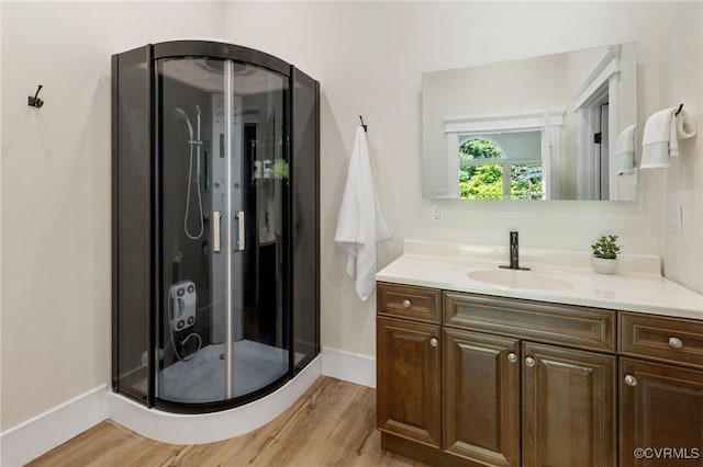 bathroom with wood finished floors, a shower stall, vanity, and baseboards