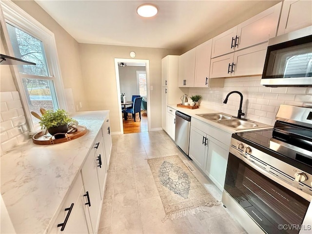 kitchen with sink, white cabinetry, appliances with stainless steel finishes, light stone countertops, and decorative backsplash