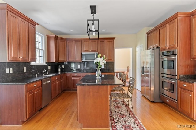 kitchen featuring light wood finished floors, tasteful backsplash, dark stone counters, a kitchen island, and appliances with stainless steel finishes