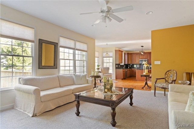 living room featuring ceiling fan, baseboards, and light colored carpet