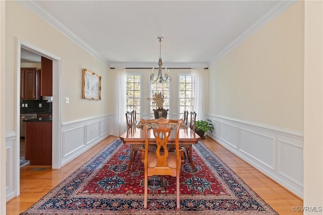 dining area with crown molding, light wood-style flooring, a decorative wall, and an inviting chandelier