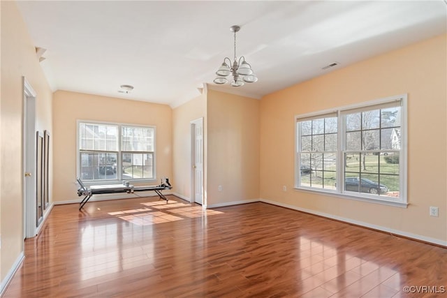 empty room with baseboards, wood finished floors, visible vents, and a notable chandelier