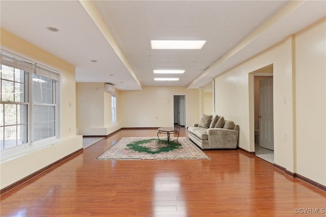 living area featuring a paneled ceiling, baseboards, and wood finished floors