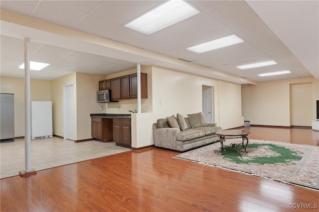 living area featuring light wood-style floors, a paneled ceiling, and baseboards