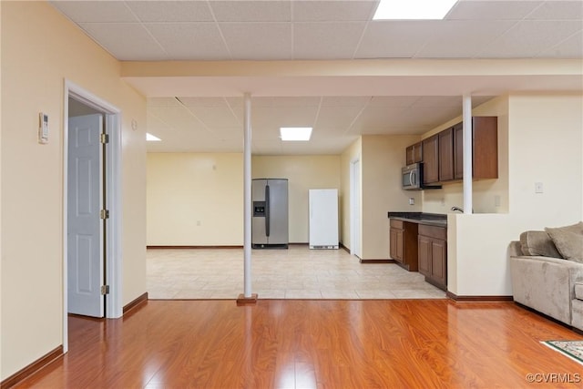 unfurnished living room with light wood-type flooring, a paneled ceiling, and baseboards