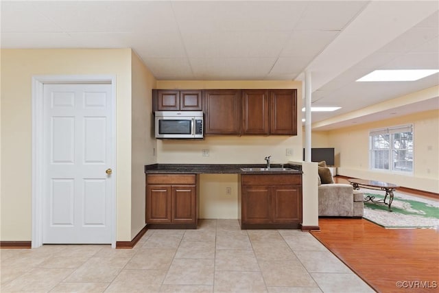 kitchen featuring light tile patterned flooring, a sink, baseboards, open floor plan, and stainless steel microwave