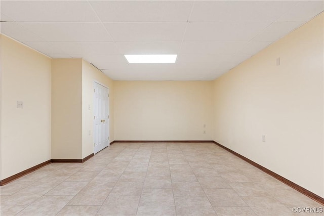 unfurnished room with light tile patterned floors, a drop ceiling, and baseboards