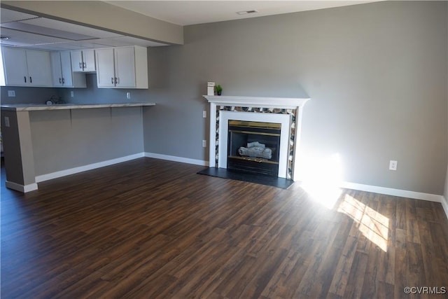 unfurnished living room with dark wood-style flooring, a premium fireplace, visible vents, and baseboards