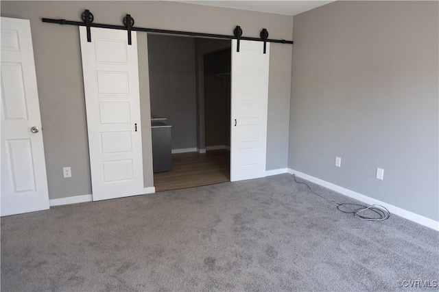 unfurnished bedroom with carpet floors, a barn door, and baseboards