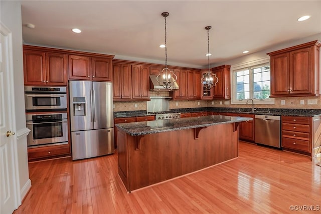 kitchen featuring a kitchen island, appliances with stainless steel finishes, decorative light fixtures, exhaust hood, and light hardwood / wood-style floors