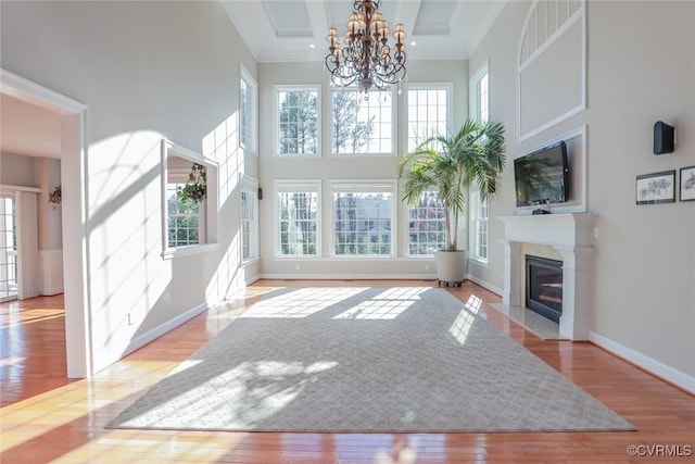 living room with an inviting chandelier, a towering ceiling, a high end fireplace, and light hardwood / wood-style floors