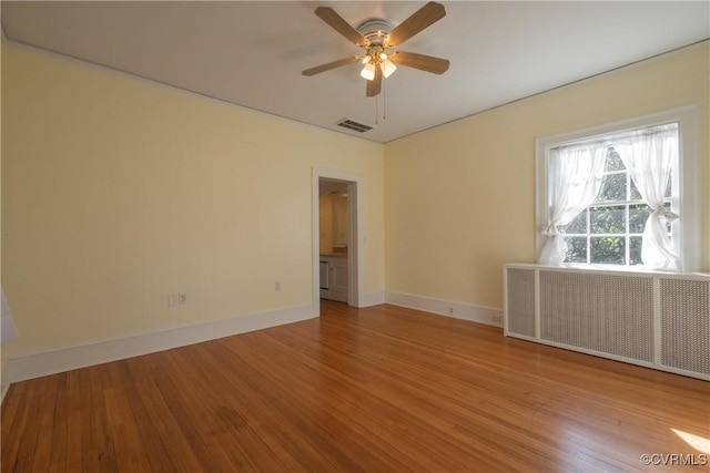 empty room with ceiling fan, light wood-type flooring, and radiator heating unit