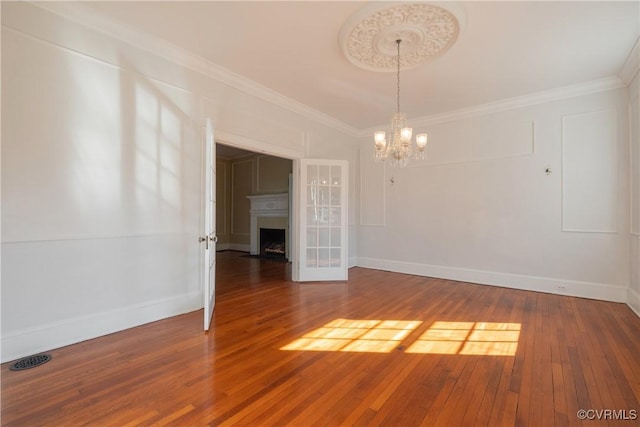 spare room with a notable chandelier, wood-type flooring, and ornamental molding