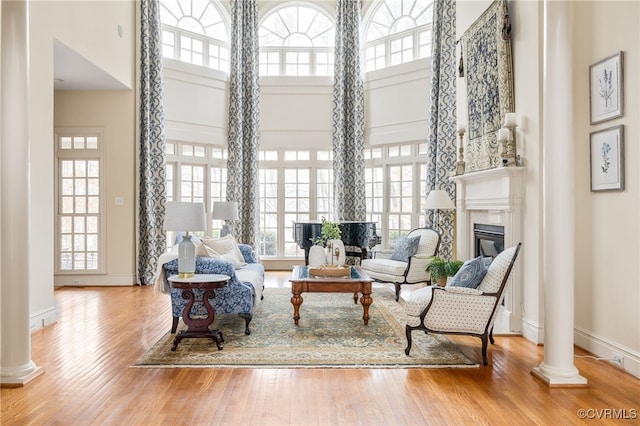 living area with wood-type flooring, a wealth of natural light, a high ceiling, and ornate columns