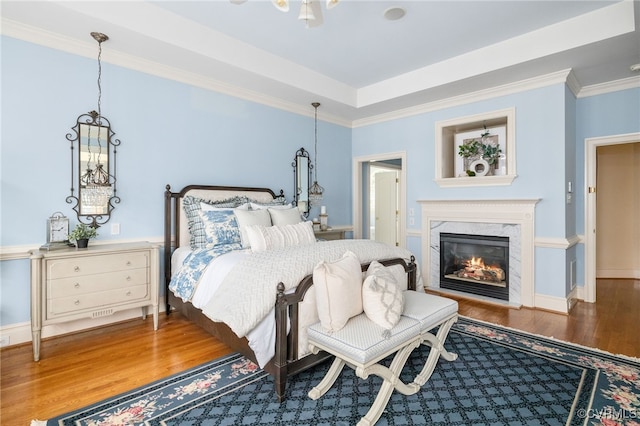 bedroom with crown molding, hardwood / wood-style flooring, a high end fireplace, and a raised ceiling