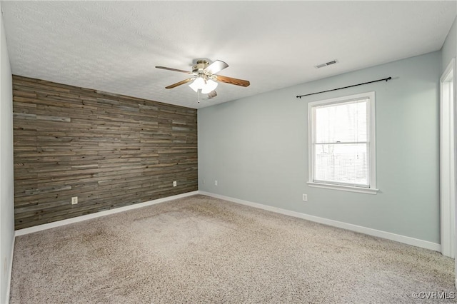 unfurnished room with ceiling fan, carpet floors, a textured ceiling, and wood walls