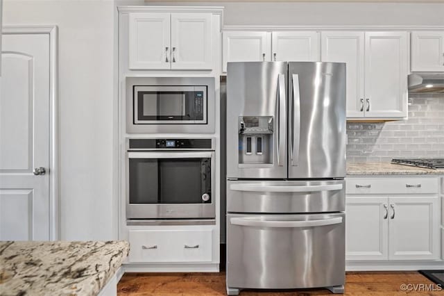 kitchen with appliances with stainless steel finishes, backsplash, white cabinetry, and under cabinet range hood