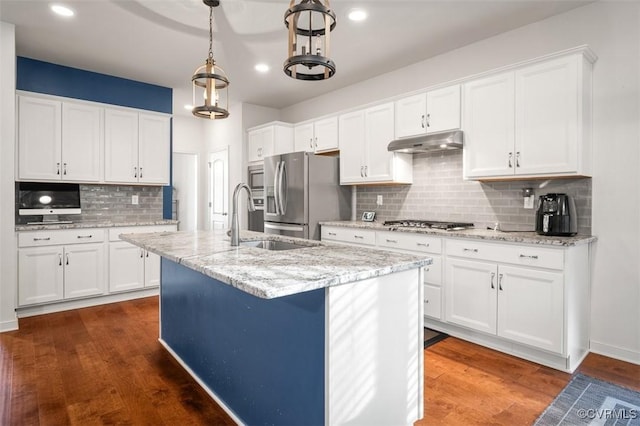 kitchen featuring under cabinet range hood, white cabinetry, appliances with stainless steel finishes, an island with sink, and dark wood finished floors