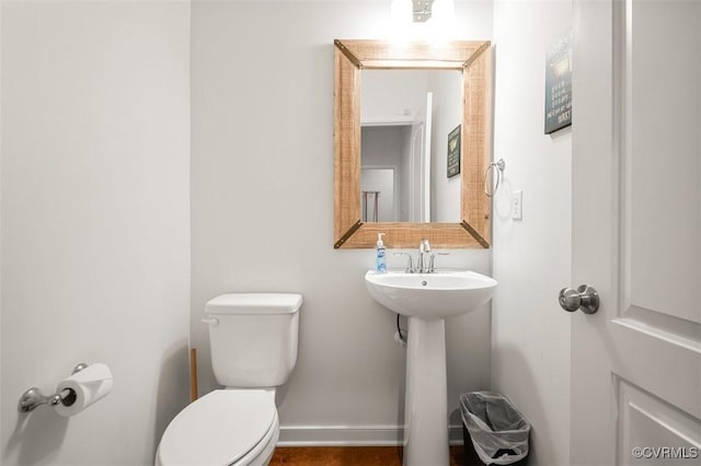 half bath featuring toilet, baseboards, and a sink