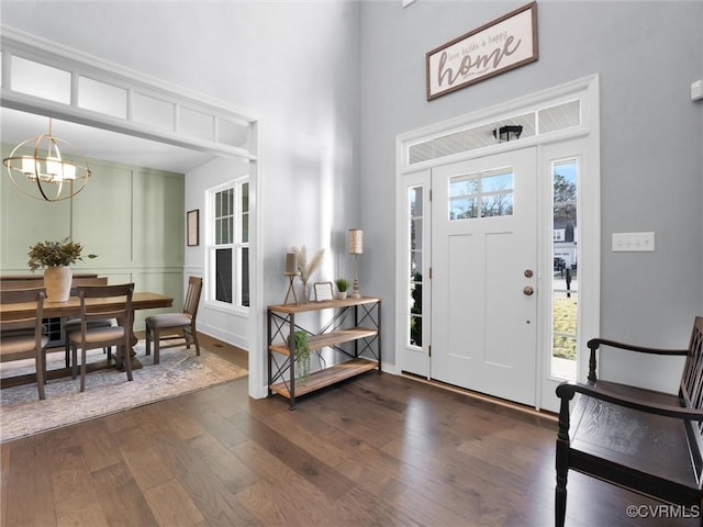 entryway featuring dark wood-type flooring, a towering ceiling, an inviting chandelier, and a wealth of natural light